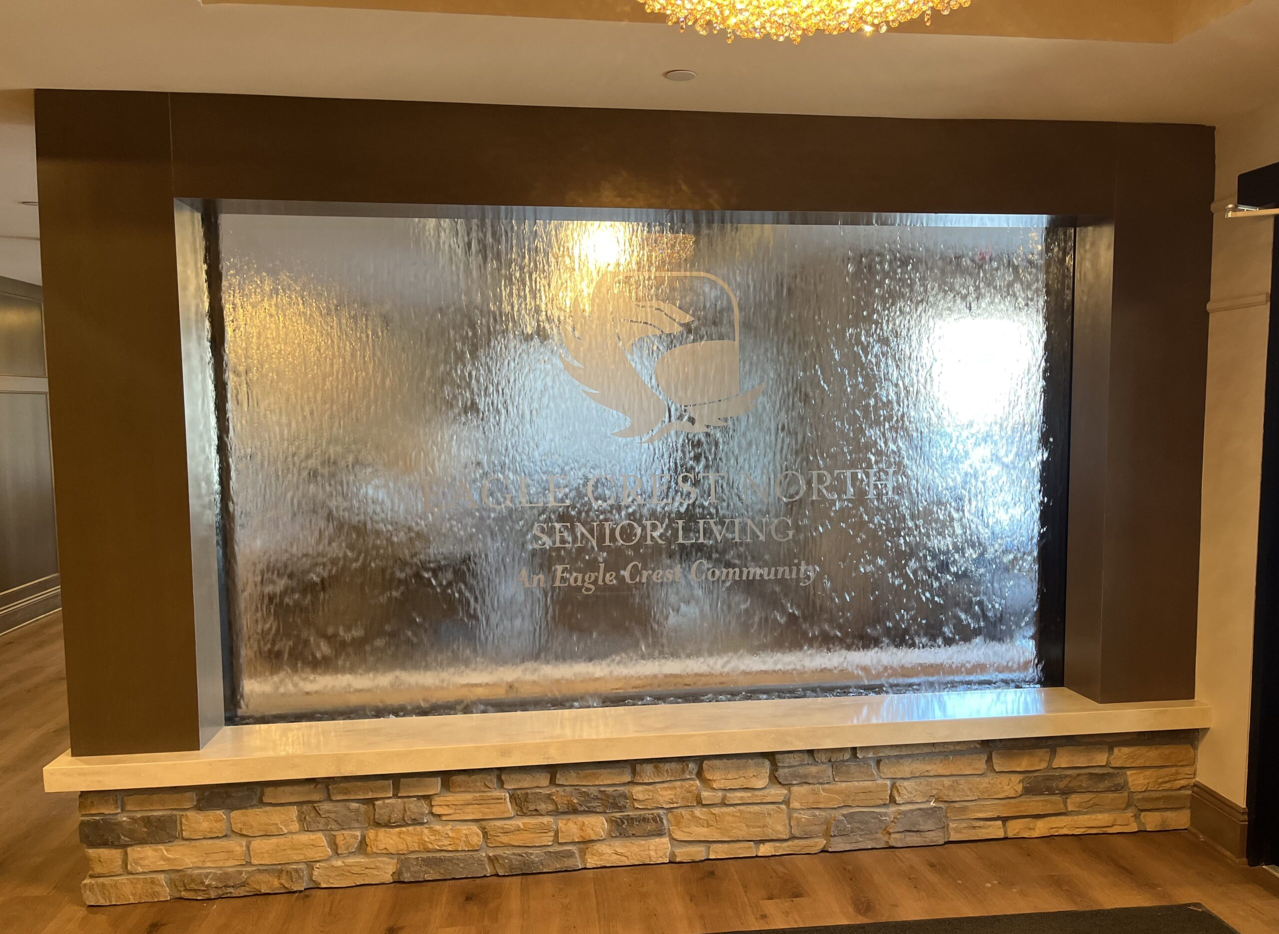 Enclosed Water Wall Waterfall with Etched Vinyl Logo at Eagle Crest North Senior Living in Onalaska, Wisconsin.