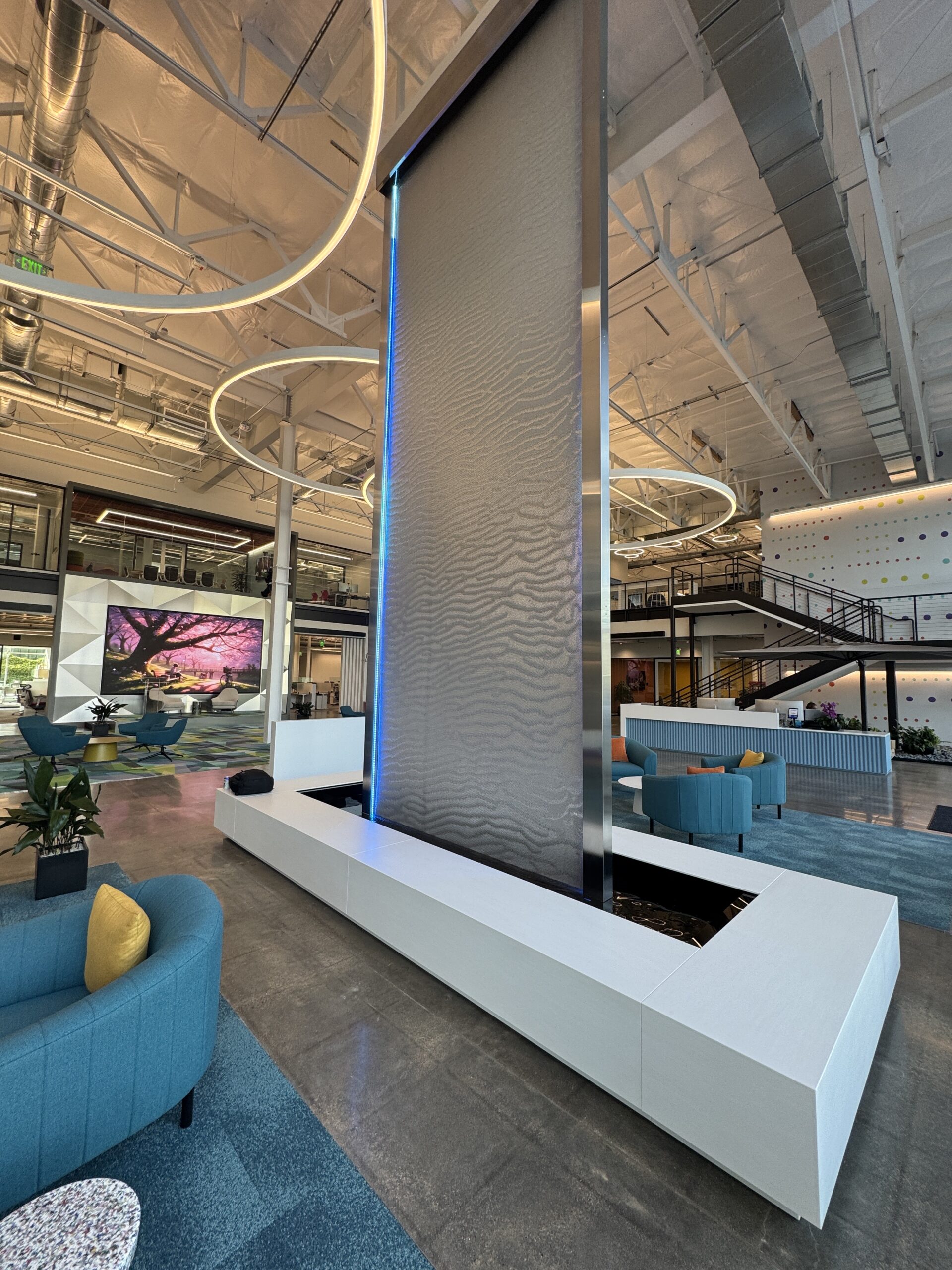 Indoor floor water fountain with illuminated water feature, modern design, surrounded by contemporary seating and vibrant decor in a spacious interior.