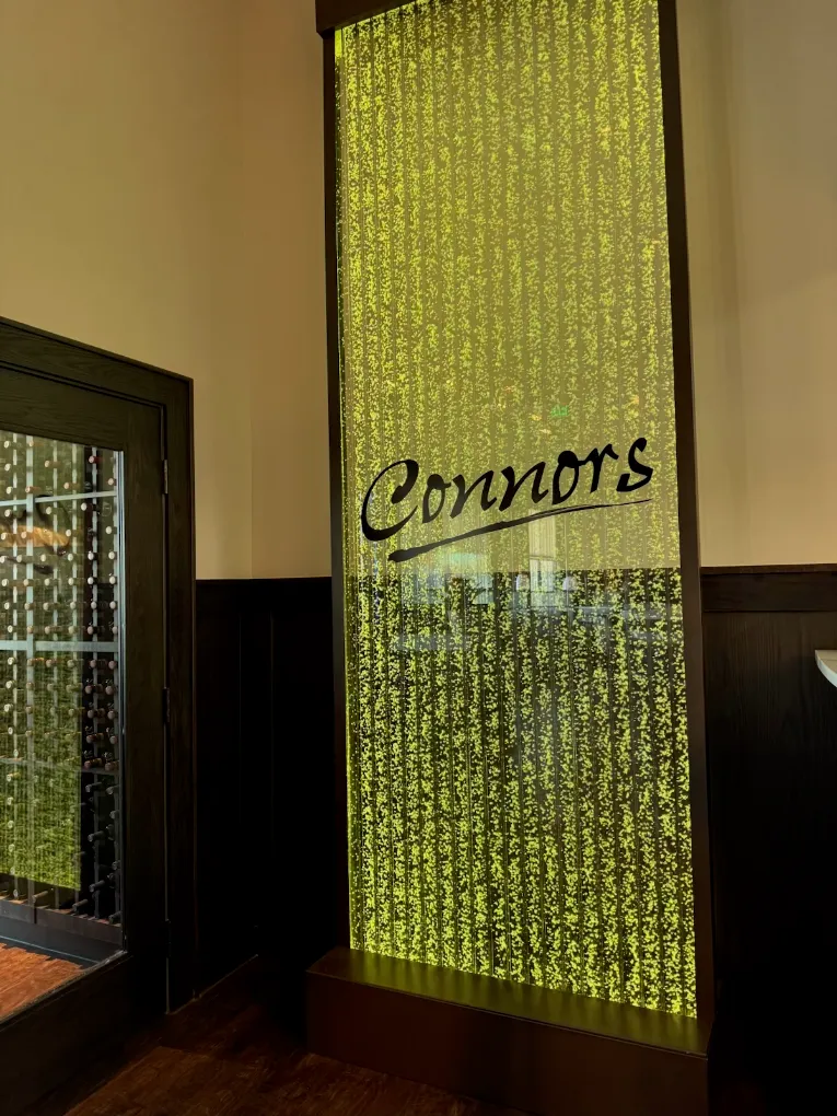 Vertical chamber bubble wall with custom logo "Connors" for Connors Steak & Seafood restaurant in Tallahassee, Florida, featuring illuminated water effect and modern design.