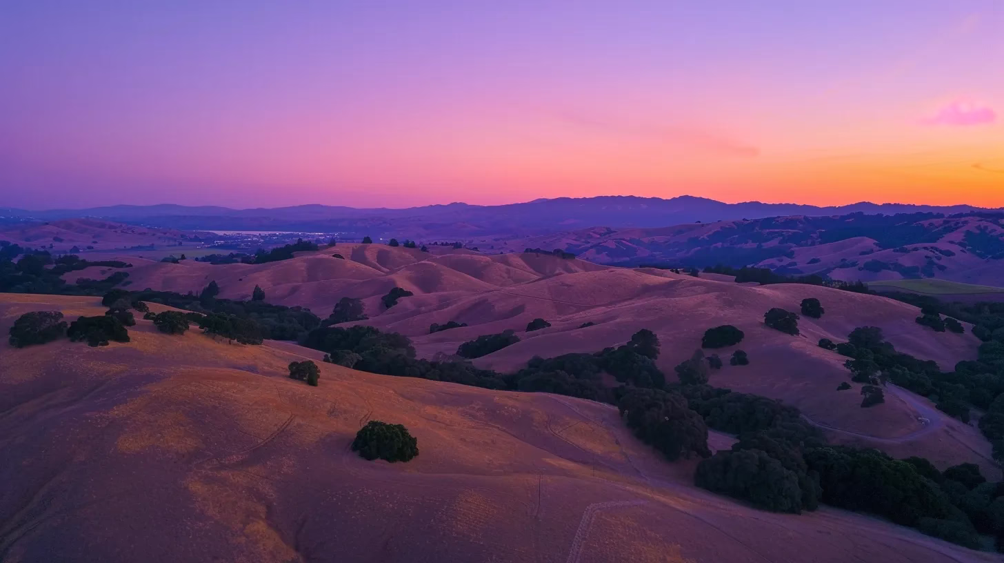 a vibrant sunset paints the sky in shades of orange and purple, casting a warm glow over a serene landscape of rolling hills and tranquil fields.